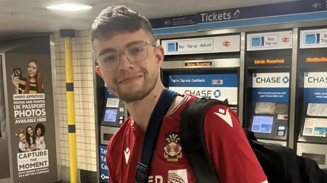 A man in a red sports shirt and his arm in a sling in the ticket hall at a London Tube station