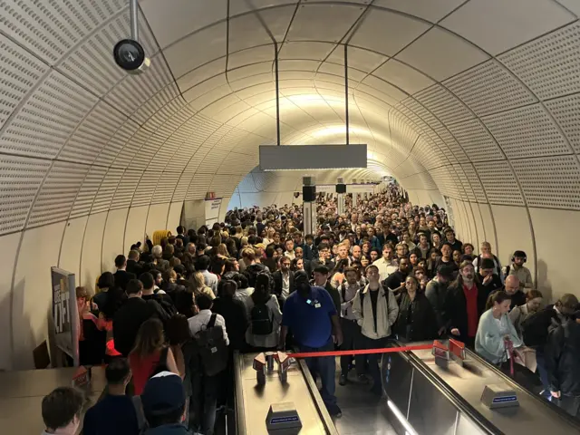 Queues, stretching back as far as the eye can see, form at the bottom of an escalator in Liverpool Street station
