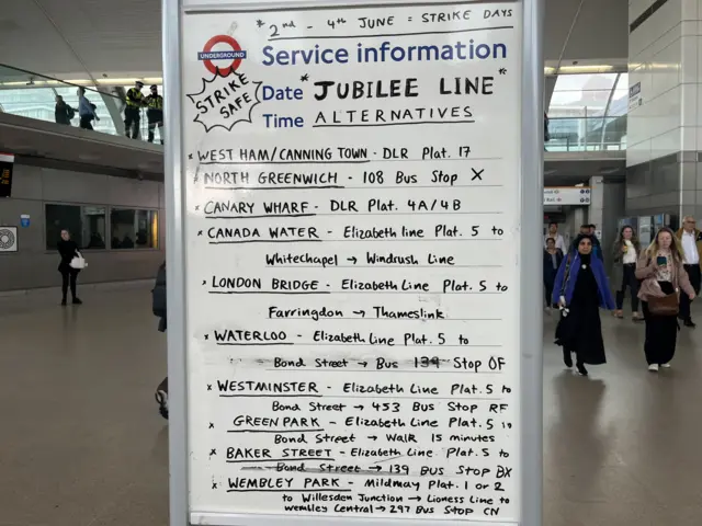 A whiteboard outlining alternative modes of transport for tube routes that has been placed in the middle of large open area in Stratford station