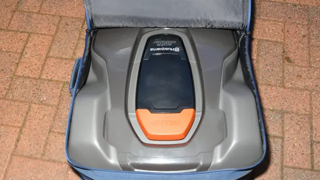 A robotic lawnmower with a brand name written on it. It is in a blue bag.
