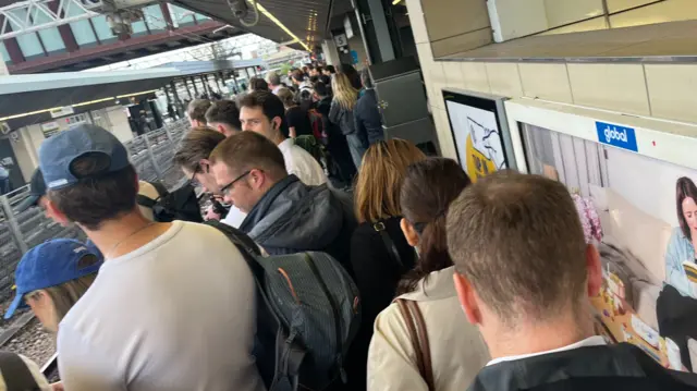 People stand almost shoulder to shoulder on a train platform as they queue for the Elizabeth line at Stratford station