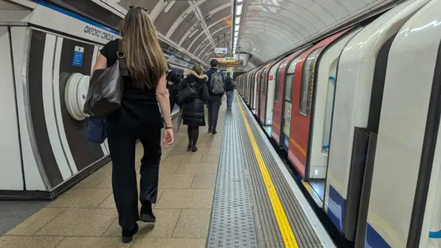A handful of people walk past a stationary tube carriage along the Victoria line tube platform at Oxford Circus