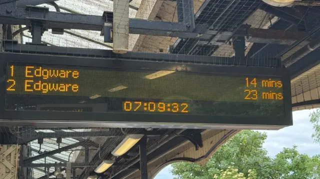 An electronic dot-matrix departure board at a London Underground station, showing the next two trains to Edgware arriving in 14 and 23 minutes, with a digital clock displaying 07:09:32.