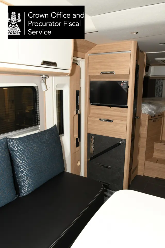 The interior of a campervan with a black sofa and cushions with a wooden interior