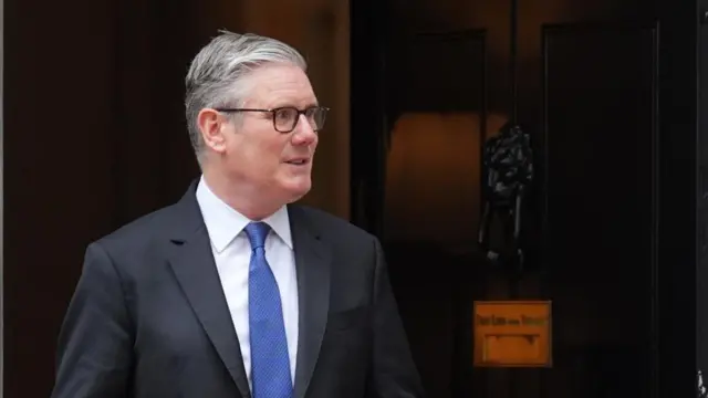 Keir Starmer stands by the door of 10 Downing Street wearing a dark suit and a blue tie