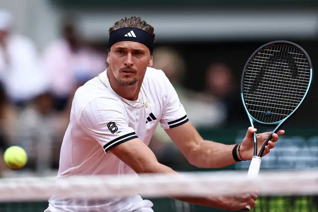 Alexander Zverev holds a tennis racquet and looks at a tennis ball