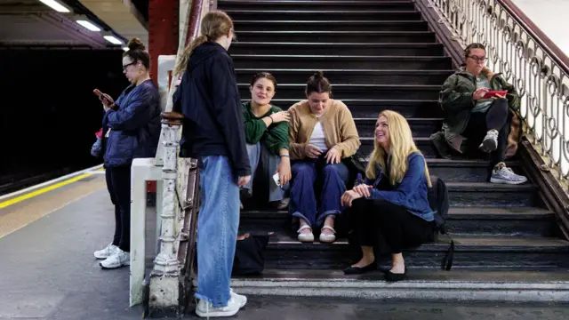 A group of women sit on stairs at an empty Tube station
