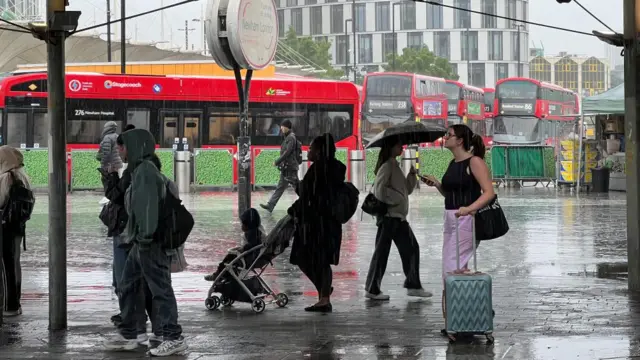Several people wait for busses in the rain