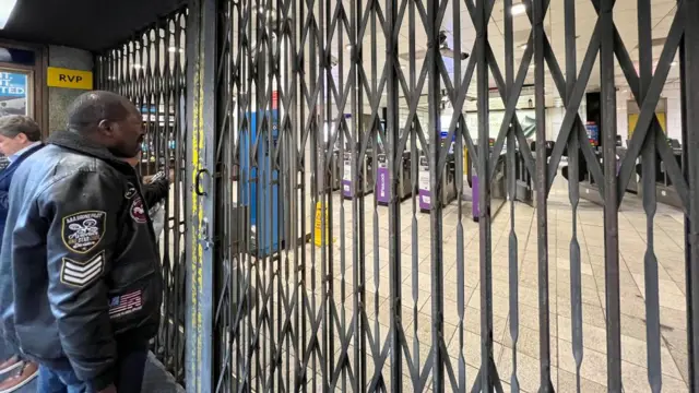 A man looks through some closed shutters at the entrance to an empty Tube station