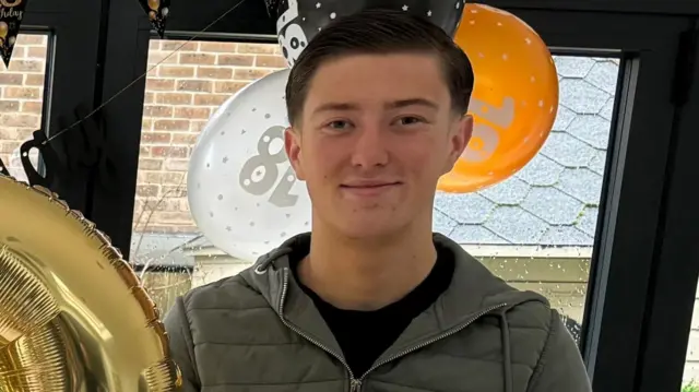 Young man stands and smiles near 18th birthday balloons