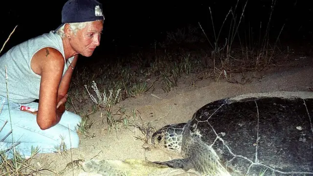 Mona Khalil, wearing a navy blue cap backwards, looks at a turtle on the coast in the southern Lebanese port city of Tyre in 2002.