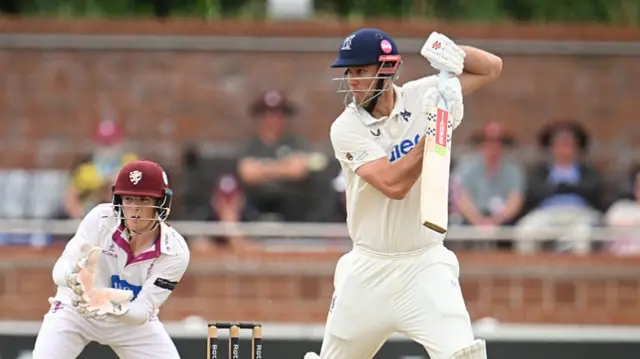 Beau Webster plays a shot as Somerset wicketkeeper James Rew looks on in the background