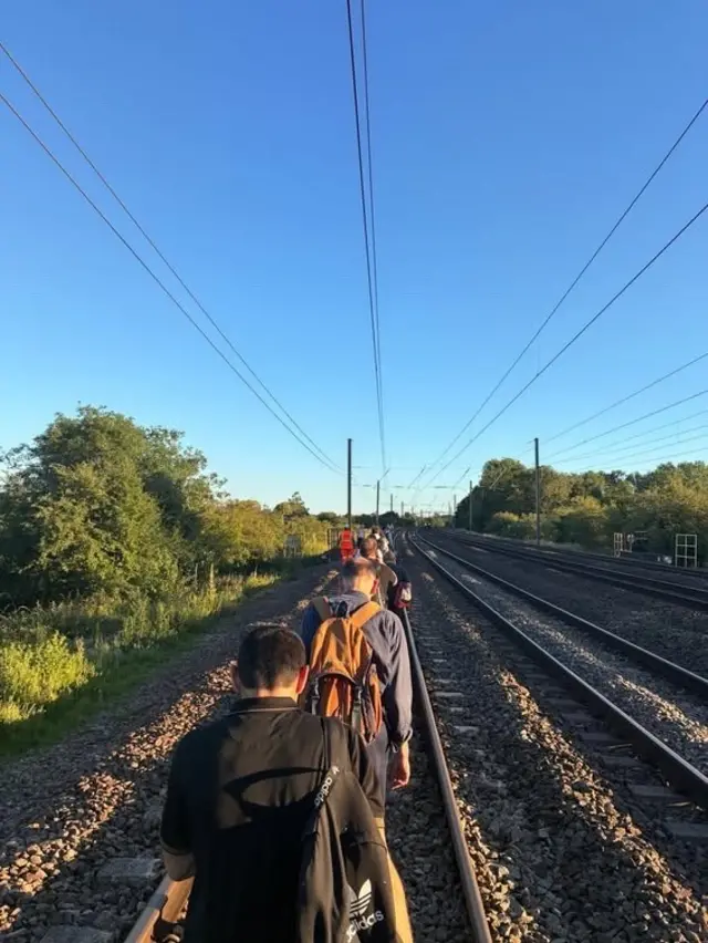 Portrait photo of people walking along train tracks after crash incident in Bedfordshire