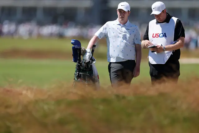 Bob MacIntyre and his caddie stand behind some long grass