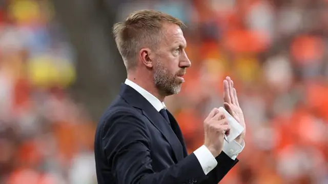 Graham Potter holds his hand up with a note in his other hand