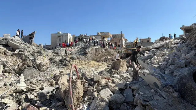 Civilians and Lebanese Red Cross personnel stand on the rubble of a damaged building after an Israeli strike on the village of Qennarit in southern Lebanon, 20 June