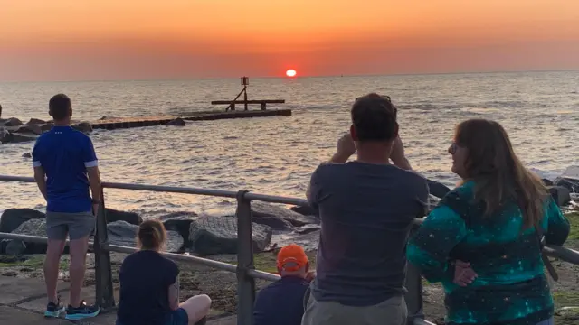 The sun rises over Ness Point is Lowestoft as people watch on
