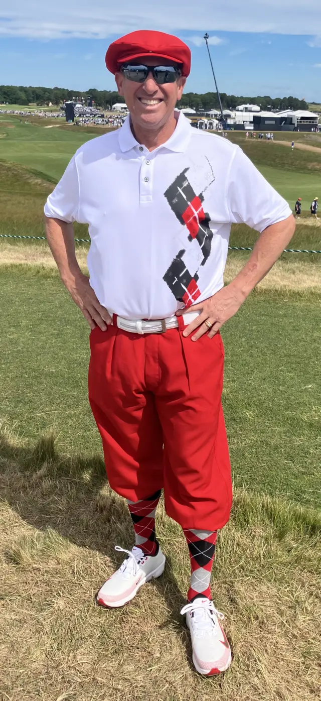 A man in a white shirt with a red flat cao, red trousers and patterned socks
