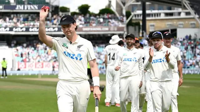 Matt Henry, wearing a white shirt and black cap, leads the New Zealand team off, holding a red ball aloft in his right hand