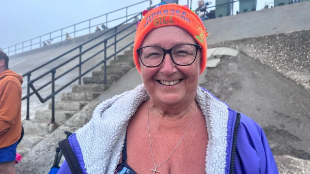 A woman wearing an orange hat and a purple jacket is smiling at the camera.