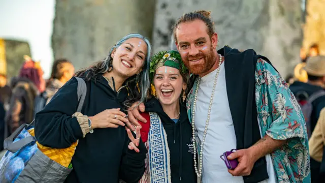 Three people smile at camera in Stonehenge