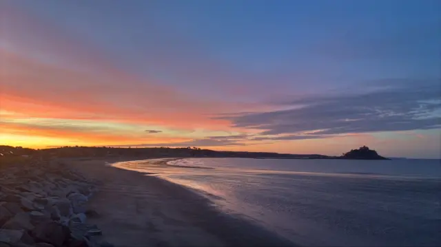 The sunrise over a sweeping beach. St Michael's Mount is in the distance on the right of the image