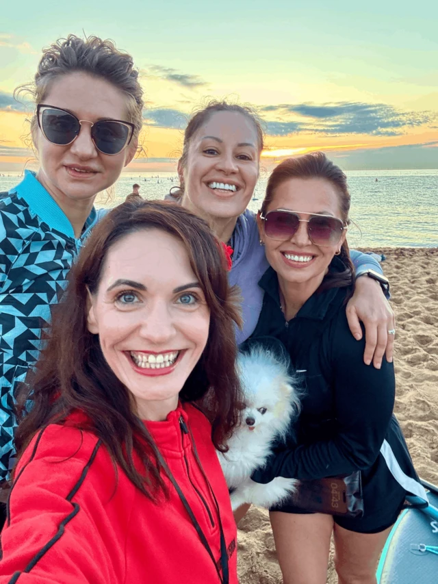Four women on a beath, with a Pomeranian dog.