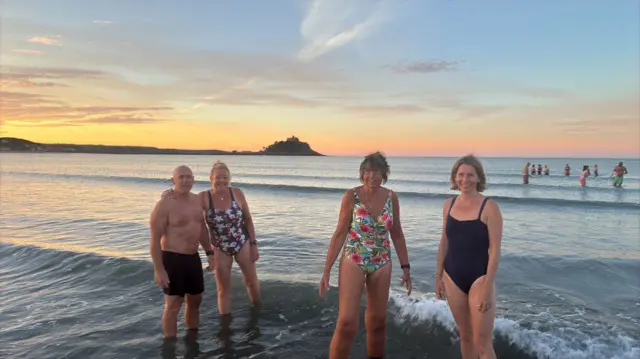 Four people are standing in the sea at sunrise.