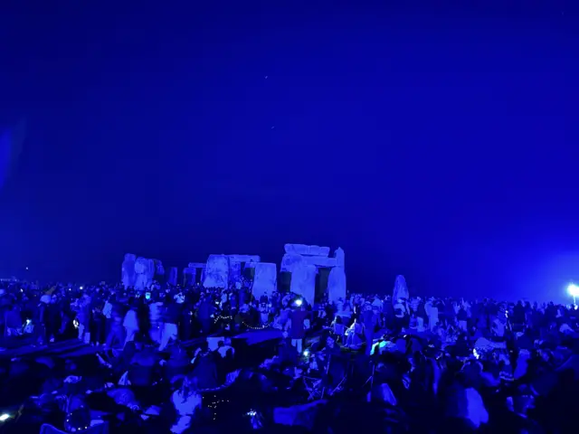 Stonehenge in the dark with people stood next to the stone circle