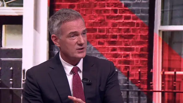 Business Secretary Peter Kyle in dark suit sits in front of a screen projecting the image of No 10