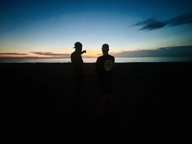 Two people are standing against the sunrise at a beach