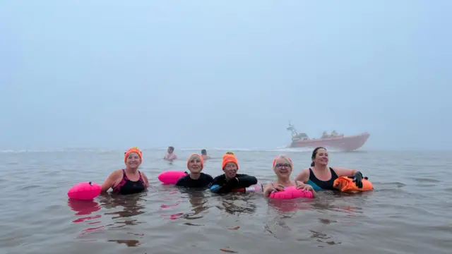 A group of women in the foggy sea.  An RNLI lifeboat is behind them.