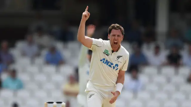 Matt Henry, wearing whites, points his right finger in the air