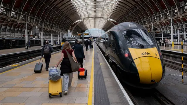 A GWR train pulling into London Paddington Station while passengers board with their luggage.