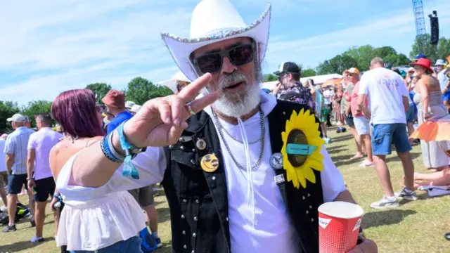 A man in a white cowboy hat and sunglasses poses for a picture in front of crowds at the Isle of Wight Festival