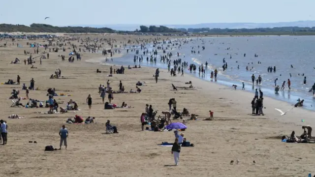 Large crowds of people enjoying the water at Weston-super-Mare beach on a sunny day.