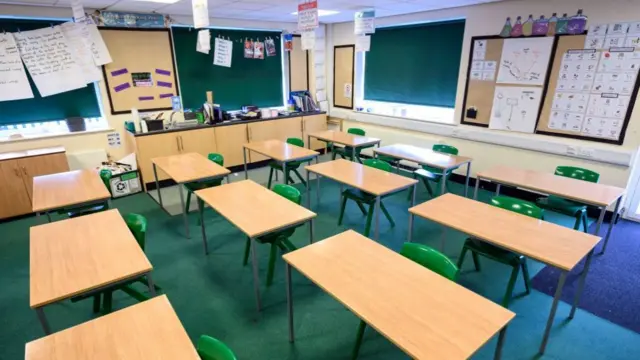 A stock image showing an empty classroom with green carpet and wooden desks.