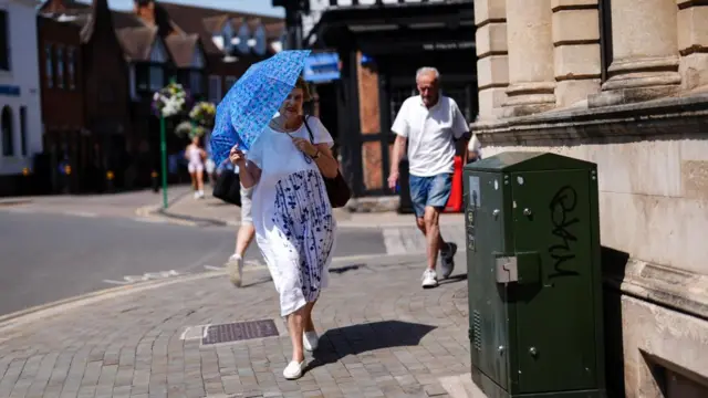 A woman uses an umbrella to shield herself from the sun while walking along the street.