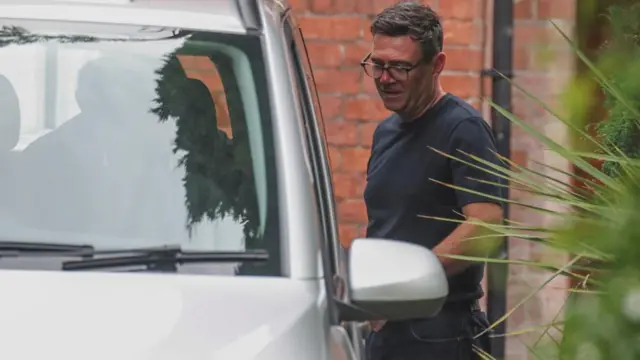 Burnham wears glasses and a black t-shirt as he is seen getting into a silver car