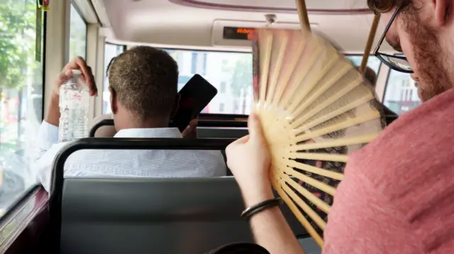 A man fans himself on a London bus.