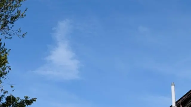 A shot of a blue sky with a cloud resembling the outline of Britain.