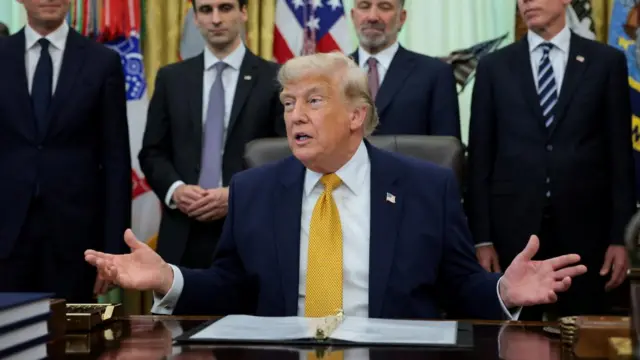 Donald Trump sits at a desk and wears a yellow tie