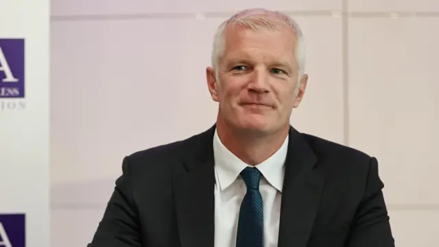 Al Carns is pictured smiling, wearing a suit and tie.