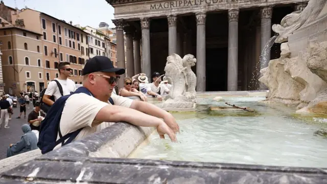 A tourist dips his hands into the cool water of the fountain in front of the historic Pantheon Basilica to escape the scorching heat in Rome, Italy on June 22, 2026.