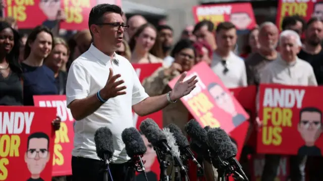 Andy Burnham is pictured speaking in Makerfield, surrounded by supporters holding placards that say 'Andy for us'