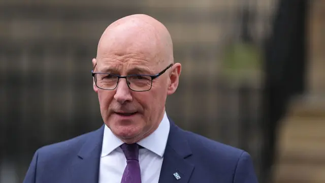 a bald man with glasses is wearing a blue suit jacket, white shirt and purple tie