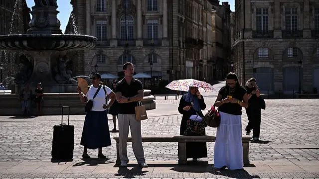 Commuters use a hand fan and an umbrella to cool down as they wait for a tramway in Bordeaux