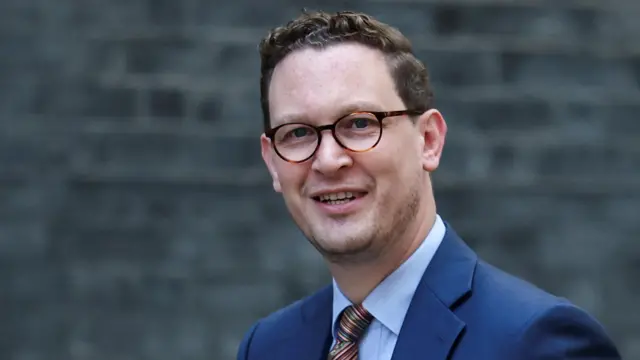 Darren Jones is pictured wearing a blue suit and tie, wearing glasses.