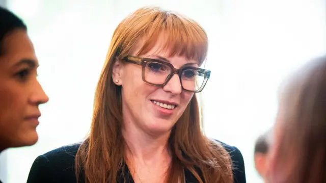 Angela Rayner is pictured speaking to several people, wearing glasses and smiling.