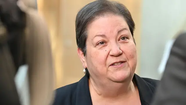 a woman with short dark hair wearing a black jacket